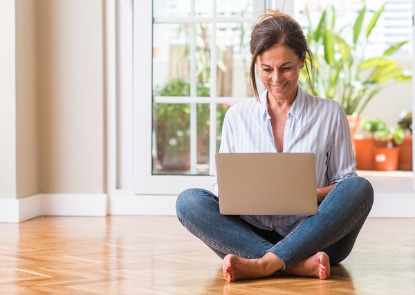 Middle aged woman using laptop at home with a happy face standing and smiling with a confident smile showing teeth